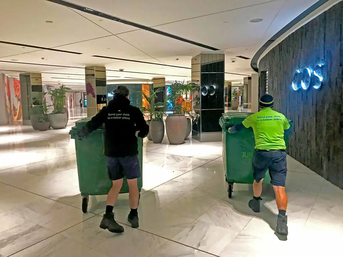 Two Junk Run removal specialists moving wheelie bins through Westfield Shopping centre in Auckland.